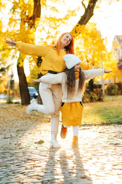 Happy family enjoying the autumn vacation at nature. Stylish family on autumn walk. Mother and daughter walking in the park. Mom and child having fun together. Autumn fashion, lifestyle and vacation.