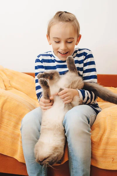 Happy kid hugging his cat. Boy relaxing on the bed with pet. Childhood, true friendship and home pet. Cute boy plays with a cat at home.