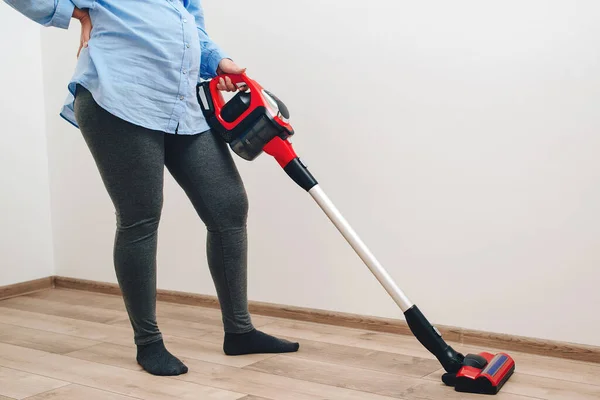Young pregnant woman enjoys cleaning her house. Modern easy cleaning. Easy cleaning with a wireless vacuum cleaner. Pregnant woman cleaning floor with handheld vacuum cleaner.