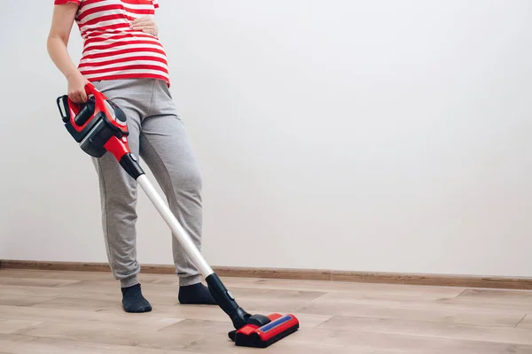 Young pregnant woman enjoys cleaning her house. Modern easy cleaning. Easy cleaning with a wireless vacuum cleaner. Pregnant woman cleaning floor with handheld vacuum cleaner.