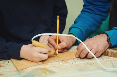 Boy burn out numbers with soldering iron on wooden disc. Kid makes wooden clock in the workshop. Young carpenter working with wood and tools in craft workshop. Woodburning, craft, school and learning