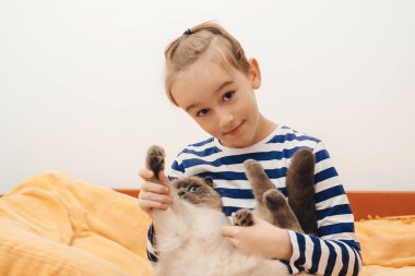 Cute boy plays with a cat at home. Happy kid hugging his cat. Boy relaxing on the bed with pet. Childhood, true friendship and home pet.