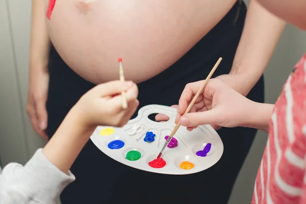 Baby birth expecting time and belly painting. Happy kids painting pregnant belly their mother. Happy children and pregnant mom having fun together at home. Family, healthy pregnancy and baby birth.