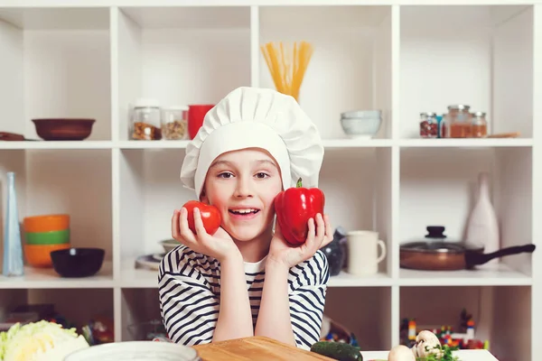 Cute boy wearing chef hat and uniform. Cooking food concept. Son preparing healthy food for family dinner. Future profession. Little chef cooking. Child holding peper and tomato.