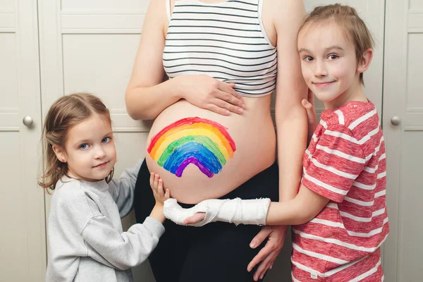 可爱的男孩和姐姐在怀孕的肚子上画彩虹 早产预产期和腹部彩绘 快乐的孩子和怀孕的妈妈在家里玩的开心 — 图库照片