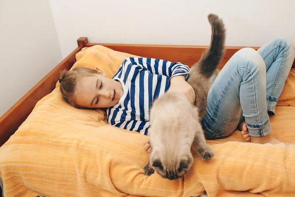 Cute boy plays with a cat at home. Happy kid hugging his cat. Boy relaxing on the bed with pet. Childhood, true friendship and home pet.