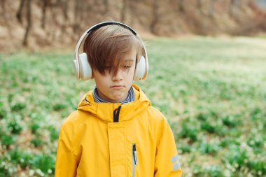 Üzgün çocuk doğada müzik dinliyor. Kulaklıklı çocuk bahar parkında dinleniyor. Kulaklık takan üzgün bir çocuk. Yaşam tarzı, çocukluk ve duygular.