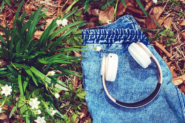 春の背景にワイヤレスヘッドフォン トップビュー ライフスタイル テクノロジーの概念 デニムジャケットの白いヘッドフォン 春の花とヘッドフォン — ストック写真