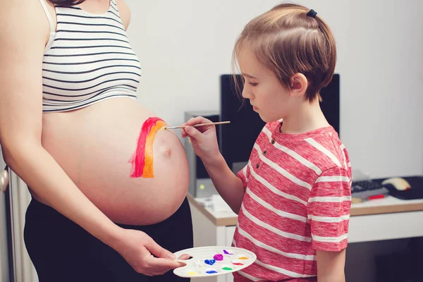 可爱的男孩在怀孕的肚子上画彩虹 他的母亲 早产预产期和腹部彩绘 怀孕的妈妈和她的儿子在家里玩得很开心 健康怀孕 — 图库照片