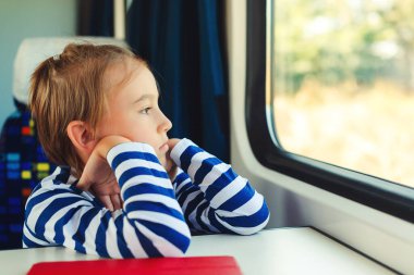 Trenin penceresinden bakan sevimli bir çocuk. Küçük çocuk trende seyahat ediyor. Çocuk trenle seyahat ediyor. Çocukluk, aile tatili, yaşam tarzı..