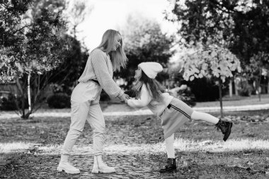 Annesiyle yürüyüş yaparken eğlenen güzel bir kız. Sonbahar tatili, yaşam tarzı. Mutlu aile parkta sonbahar havasının tadını çıkarıyor..