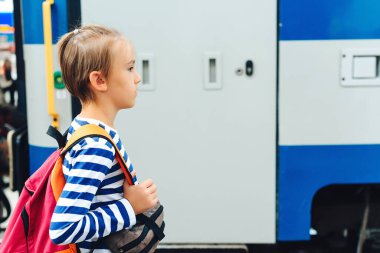Çocuk tren istasyonunda ekspres tren bekliyor. Metroda sırt çantalı bir çocuk. Seyahat, turizm, tatil ve aile kavramı.