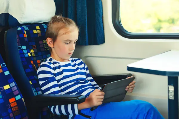 Cute child playing video games online on tablet during trip. Kid travels on a train. Childhood, family vacation, lifestyle. Journey. Gadget addiction.