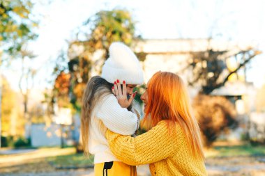 Annesiyle sonbahar yürüyüşünde kucaklaşan güzel bir kız. Sonbahar tatili, yaşam tarzı. Mutlu aile sonbahar parkında oynuyor..