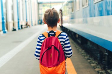 Çocuk tren istasyonunda ekspres tren bekliyor. Metroda sırt çantalı bir çocuk. Seyahat, turizm, tatil ve aile kavramı.