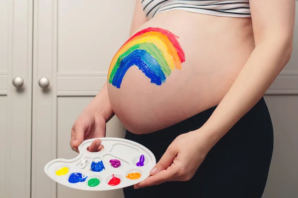 Belly painting, rainbow. Pregnant woman holding belly with painting. Waiting for baby concept. Belly painting and maternity photo. Happy family expecting baby birth.