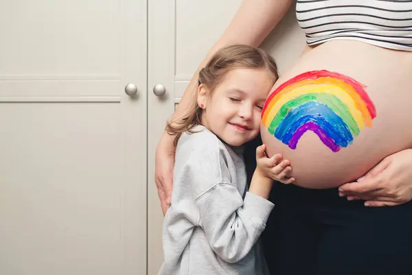 Family, healthy pregnancy and baby birth. Sweet little daughter painting pregnant belly her mother. Baby birth expecting time and belly painting.