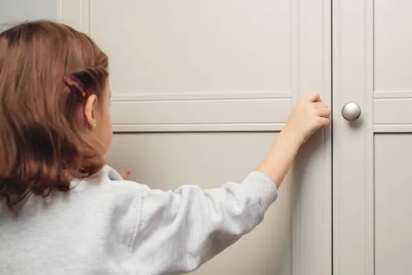 Little girl opens the cupboard. Cute baby girl playing with a wooden cupboard. Toddler baby opens the closet door in the home living room. A small child opens a shelf drawer.
