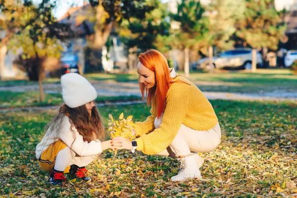 Happy family enjoying autumn day together. Family autumn walk. Autumn holidays, lifestyle, childhood. Mother and child girl playing with autumn leaves.