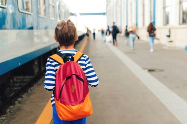 Çocuk tren istasyonunda ekspres tren bekliyor. Metroda sırt çantalı bir çocuk. Seyahat, turizm, tatil ve aile kavramı.