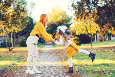 Annesiyle yürüyüş yaparken eğlenen güzel bir kız. Sonbahar tatili, yaşam tarzı. Mutlu aile parkta sonbahar havasının tadını çıkarıyor..