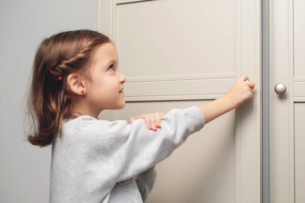 Маленькая девочка открывает шкаф. Милая девочка играет с деревянным шкафом. Маленький ребенок открывает ящик на полке.
