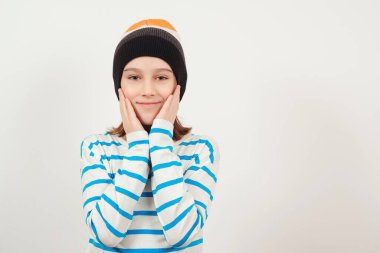 Beyaz arka planda gülümseyen kendine güvenen şık bir çocuk. Yünlü şapka takan sevimli bir adam. On bir yaşındaki bir çocuğun portresi. Yaşam tarzı, moda ve insanlar.