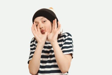 Heyecanlı çocuk stüdyoda eğleniyor ve poz veriyor. On bir yaşındaki bir çocuğun portresi. Şık yün şapka ve tişört giyen bir çocuk. Yaşam tarzı, insanlar, duygu konsepti.