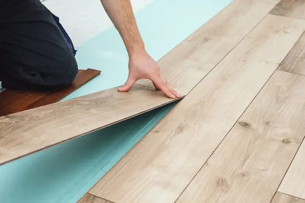 Man laying laminate flooring - closeup on male hands. Worker hands installing timber laminate floor. Easy and quick installation of the flooring. Connecting laminate locks. DIY floating floor.