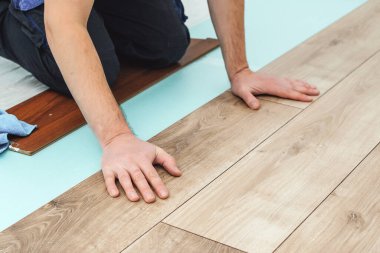 Döşeme kaplaması döşeyen adam, erkek ellerine yakın plan. İşçi elleri kereste kaplama döşemesi kuruyor. Döşemelerin kolay ve hızlı kurulumu. Kaplama kilitler bağlanıyor. Yüzen zemin.