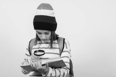 Çocuk büyüteçten kitaba bakıyor. Öğrenci elinde büyüteç tutuyordu. Çocukların ilgisi. Büyüteçli öğrenci portresi. Okul, öğrenme ve geliştirme kavramı.