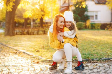 Sonbahar yürüyüşünde gülen sevimli bir aile. Sonbahar tatili, yaşam tarzı. Mutlu küçük kız ve annesi sonbahar parkında oynuyorlar..