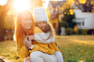 Mutlu küçük kız ve annesi sonbahar parkında oynuyorlar. Sonbahar yürüyüşünde gülen sevimli bir aile. Sonbahar tatili, yaşam tarzı.
