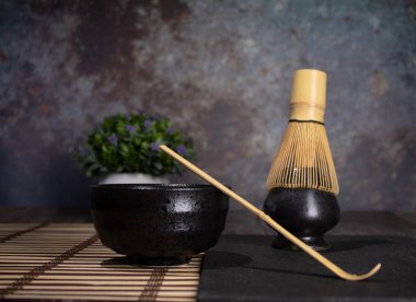 Siyah kibrit çay kasesi, gri lekeli gri çırpı ve bambu kaşıklı masa örtüsü, yeşil çay, yeşil çay, çimento, ön plan lekeli, spac manzaralı lokanta fotoğrafı.