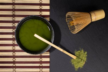Bir kase siyah kibrit çayı, gri lekeli çırpı ve bambu kaşıklı masa örtüsü yeşil çaylı eski çimento arka planı lekeli, üst manzaralı, metin için yeri olan. 
