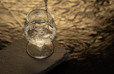 Bardakta temiz likör, anis, tekila, rom, vb. Tahta bir taşın üzerinde cam ve altın yansımalı bir su tabanında. metin için boşluk ile,