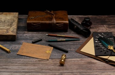 Antik papirüs yaprakları günlüğü. Kalemli ve kabartmalı kapaklar. Mürekkep şişesi, defter, kalem uçları, kalemler, mühür, zarf, balmumu, mektup açacağı, pul, zarf, balmumu.