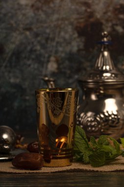 Çayla doldurulmuş ve içeriden aydınlatılmış Arapça motifli bir bardağın dikey fotoğrafı ve kahverengi şeker veya nane şekerli gümüş tabaklar ve tabaklardan birinde koyu renkli bir fotoğraf.