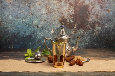 Arap desenli fincanlar ve çaydanlık çay ve nane ile dolu, çay ve kamış şekeri ahşap bir masa üzerinde iki tabak üzerinde kaba bej bir iplik ve eski çimento gibi lekelenmiş bir arka plan, metin için yer var.