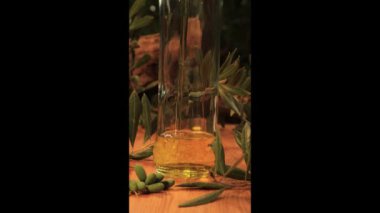 Ekstra zeytinyağı cam bir şişeye dökülüyor, yakın çekim köpürüyor, etrafında yapraklar ve zeytinlerle, ahşap masa ve arka planda eski zeytin gövdeleri ve yazı için yeri var. dikey video