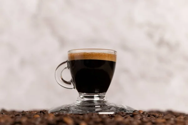 espresso or black coffee in a clear cup on a coffee bean table with a gray marble-grained marble background with space for text