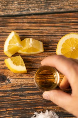 Bir elinde rom, viski, tuz ve limon dilimleri ya da siyah arka planı olan ahşap bir masanın üzerindeki dilimler olan shot bardağı..