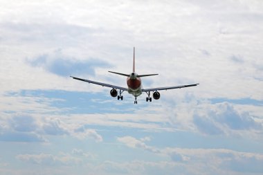 Yandan bir uçak iniş için yaklaşıyor, bulutların arka planına karşı..