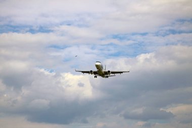 Yandan bir uçak iniş için yaklaşıyor, bulutların arka planına karşı..