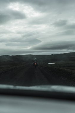 İzlanda 'nın dağlık kesimlerinde toprak üzerinde motosiklet süren bir motosiklet. Arabanın ön camından vurulmuş.