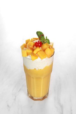 Mango parçaları, kiraz ve nane yapraklarıyla süslenmiş sarı mango suyu. Beyaz arkaplan ve koyu ahşap