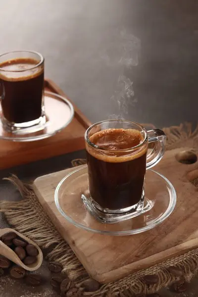 black coffee is served in a clear cup with a wooden base