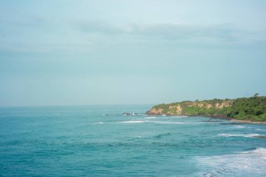 Büyük deniz dalgalarıyla yeşil bir uçurumdan sahilin manzaralı manzarası. Santolo Plajı, Batı Java, Endonezya