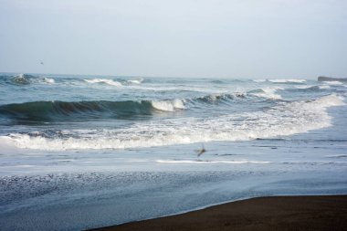 Güçlü köpüklü deniz dalgaları bulutlu mavi gökyüzüne doğru yuvarlanıyor ve sıçrıyor.