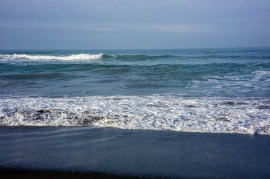 Güçlü köpüklü deniz dalgaları bulutlu mavi gökyüzüne doğru yuvarlanıyor ve sıçrıyor.